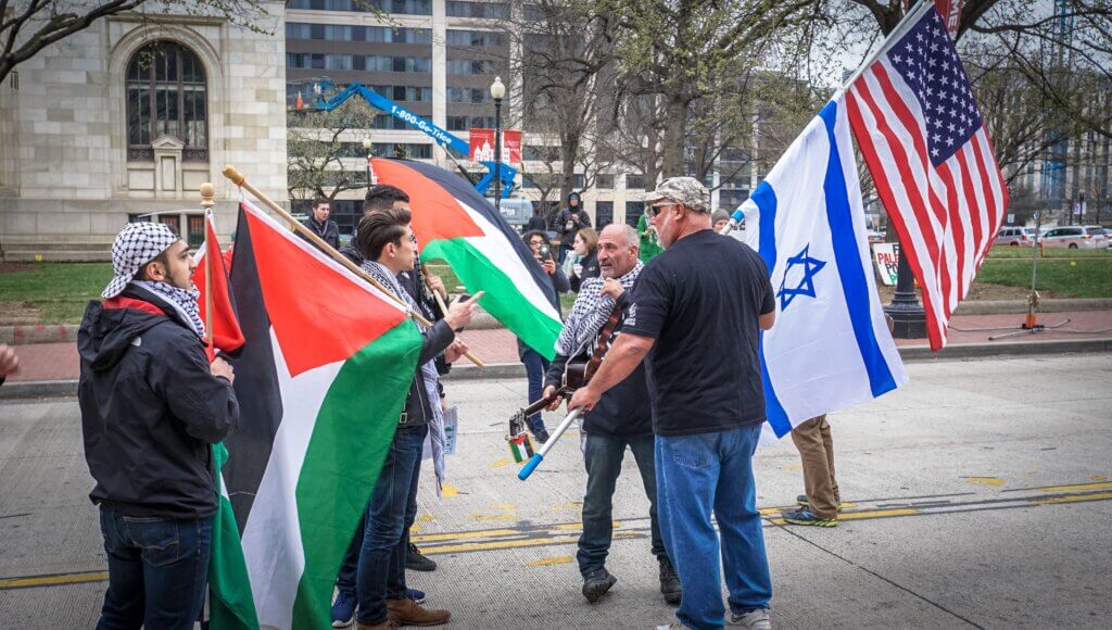 Photo shows protesters carrying Palestinians flags during an argument with counter-protesters carrying Israeli and American flags.