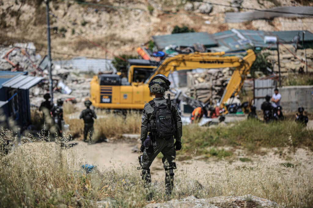 An Israeli soldier stands guard as bulldozers carry out a demolition operation in the background in the Jabal Mukaber neighborhood of East Jerusalem, May 10, 2023.