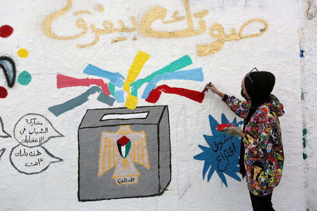 A girl in Gaza paints a mural depicting a ballot box with an eagle symbol painted on it, with a Palestinian flag emblazoned on the eagle's chest and the word 