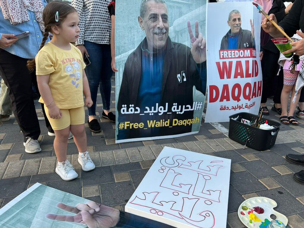 Milad Daqqa, left, standing next to a poster depicting her father, Walid Daqqa, holding up the victory sign with the sentence 